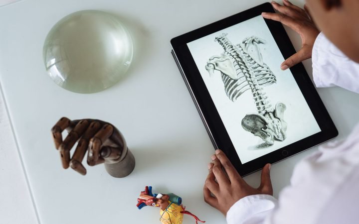 Médico estudando a anatomia da coluna vertebral em um tablet, com modelos anatômicos sobre a mesa