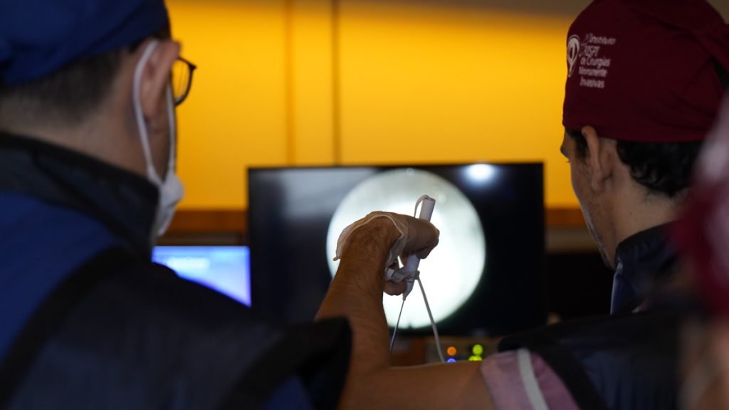 Instrutor do EndoColuna orienta aluno durante cirurgia endoscópica da coluna, com a imagem do endoscópio no monitor