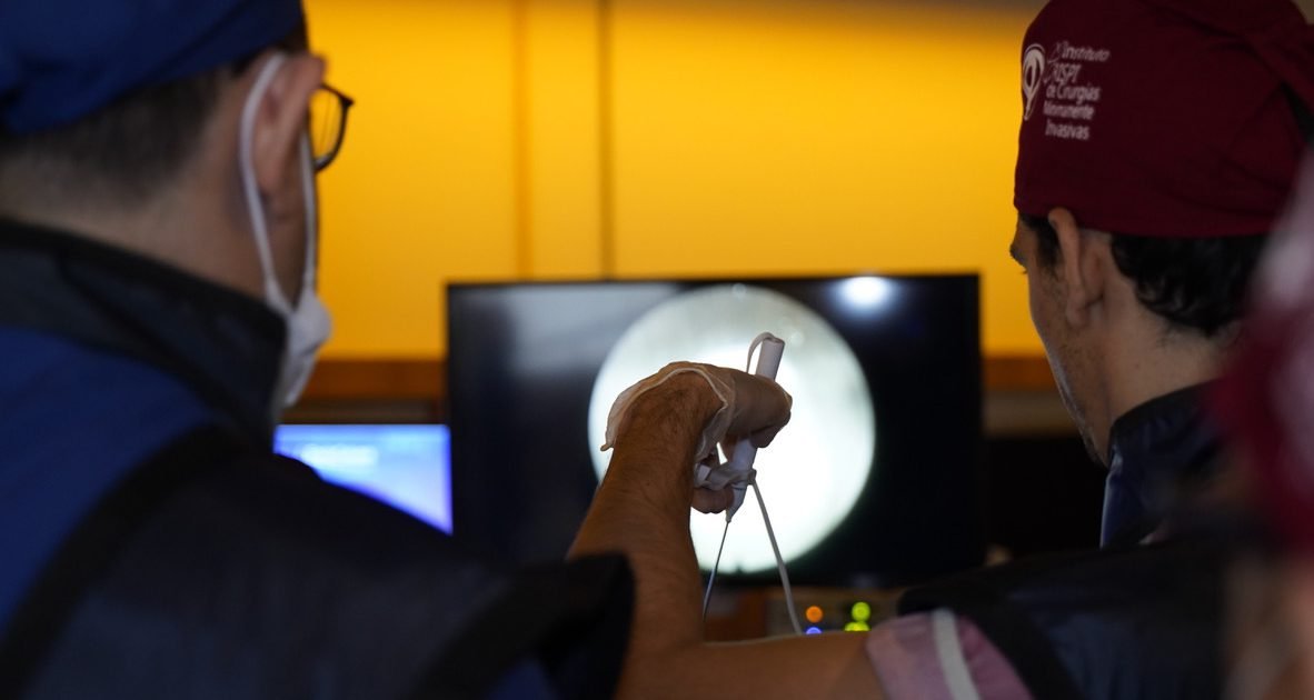 Instrutor do EndoColuna orienta aluno durante cirurgia endoscópica da coluna, com a imagem do endoscópio no monitor