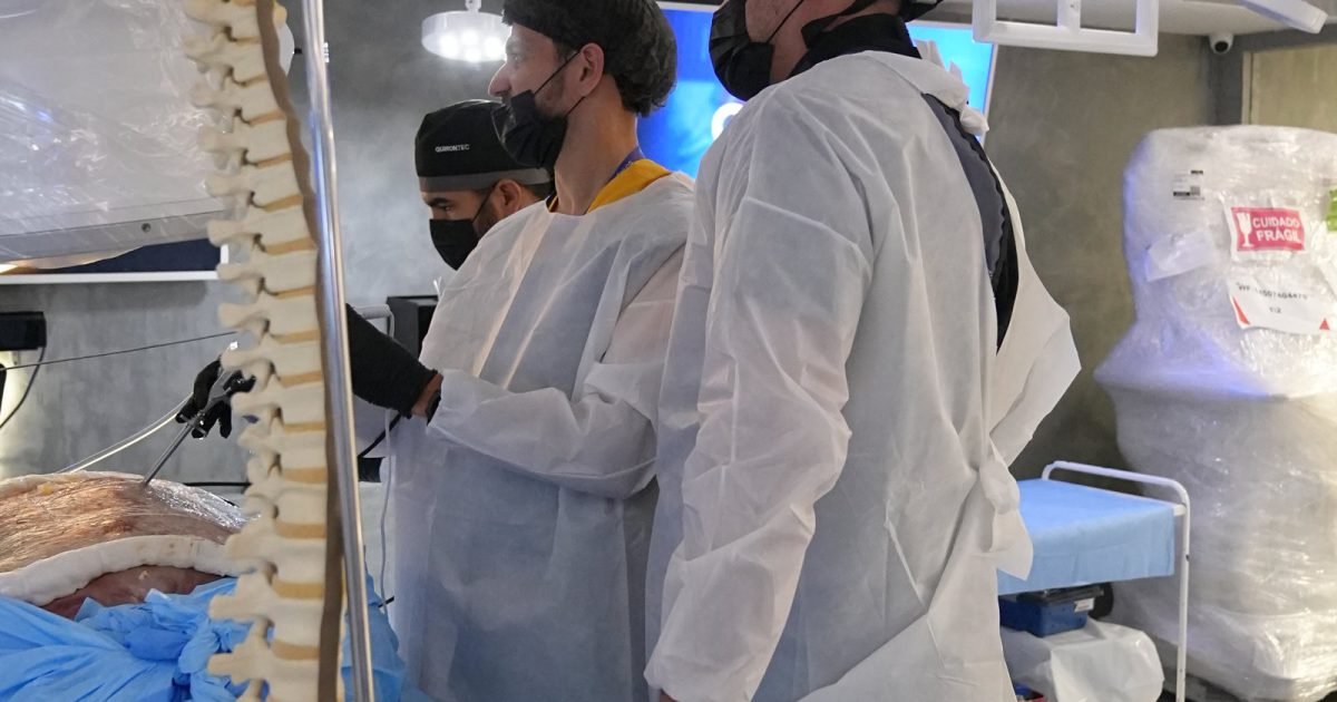 Instrutor do EndoColuna ao lado de modelo de coluna no laboratório do Cadaverlab