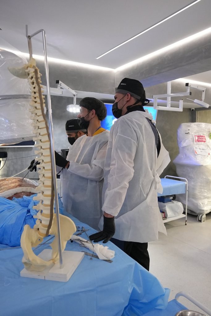 Instrutor do EndoColuna ao lado de modelo de coluna no laboratório do Cadaverlab