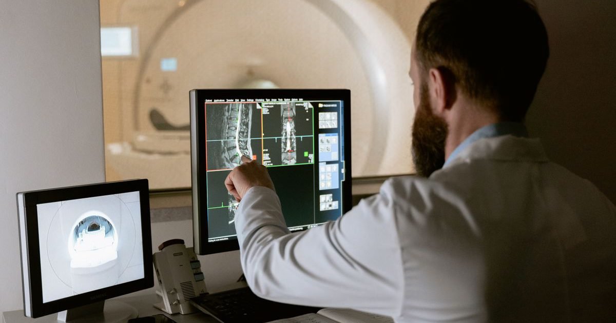 Médico analisando imagens de ressonância magnética da coluna em monitores
